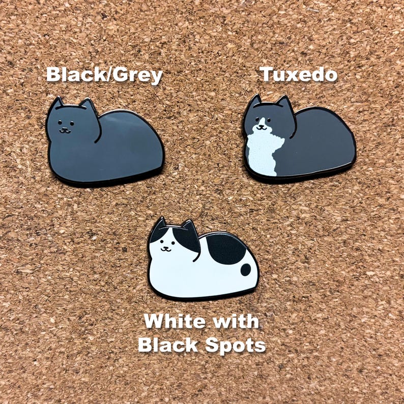 May include: Three enamel pins featuring different cat designs. The first pin is a black and gray cat, the second pin is a tuxedo cat, and the third pin is a white cat with black spots. The pins are labeled "Black/Grey", "Tuxedo", and "White with Black Spots".