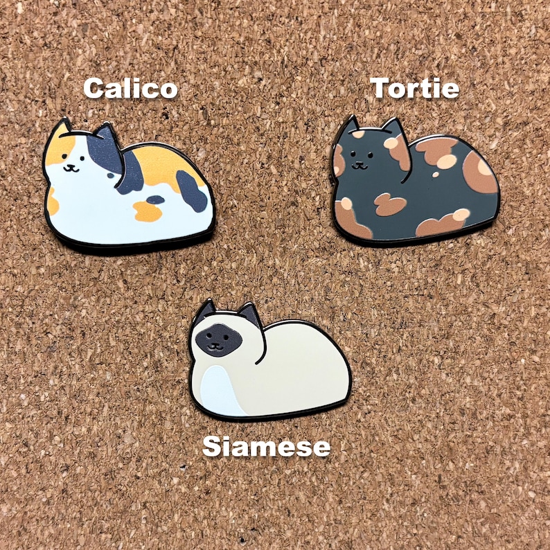 May include: Three enamel pins featuring different cat breeds. The pins are in the shape of cats and are labeled "Calico", "Tortie", and "Siamese".