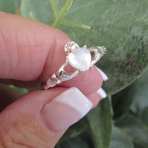 May include: A silver ring with a white heart-shaped mother of pearl stone. The ring is a Celtic knot design.