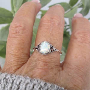 May include: A silver ring with an oval-shaped white opal gemstone set in a delicate filigree design.