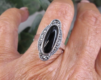 May include: A silver ring with a black oval gemstone surrounded by marcasite stones.