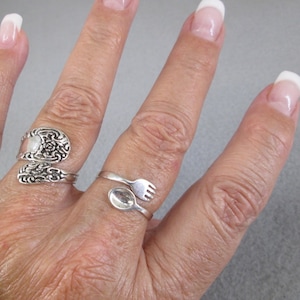 May include: Two silver rings, one with a spoon design and the other with a fork design, worn on a person's finger.