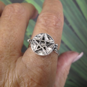 May include: A silver ring with a pentagram design. The ring is worn on a finger.