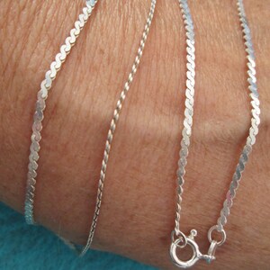 May include: Four silver chains of different styles, including a rope chain, a box chain, and two herringbone chains. The chains are layered on a person's wrist and have a lobster clasp.