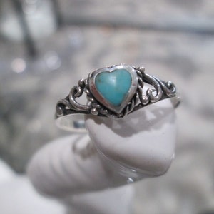 May include: A silver ring with a heart-shaped turquoise stone. The ring has a delicate, ornate design.