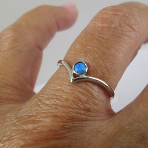 May include: A silver ring with a blue opal gemstone set in a V-shaped band.