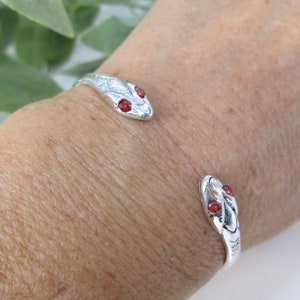 May include: Silver snake bracelet with red gemstone eyes. The snake is curled around the wrist.