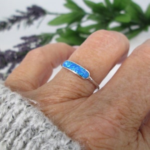May include: A silver ring with a blue opal stone set in a rectangular shape.