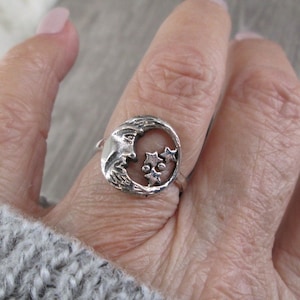 May include: A silver ring with a crescent moon design and three stars. The ring is on a person's finger.