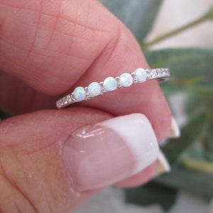 May include: A silver band ring with a row of white opal stones set in a pave setting.