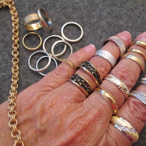 May include: A gold chain necklace with a decorative pattern and a variety of silver and gold rings on a hand.