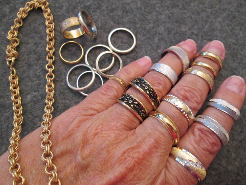May include: A gold chain necklace with a decorative pattern and a variety of silver and gold rings on a hand.