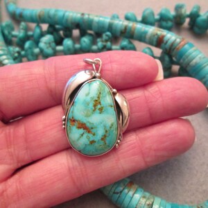 Peut inclure: Un pendentif en turquoise avec un sertissage en argent. La turquoise est de couleur bleu clair avec des veines brunes. Le pendentif est suspendu &agrave; une cha&icirc;ne en argent.