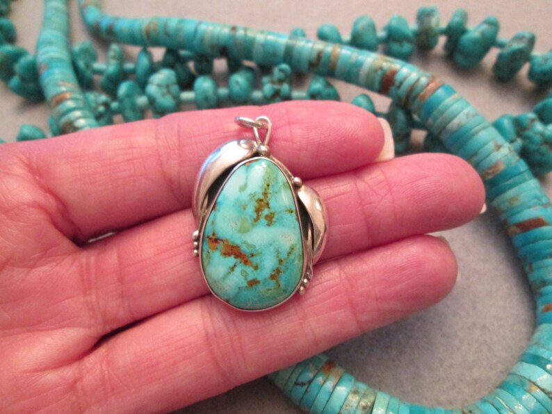 Peut inclure: Un pendentif en turquoise avec un sertissage en argent. La turquoise est de couleur bleu clair avec des veines brunes. Le pendentif est suspendu &agrave; une cha&icirc;ne en argent.