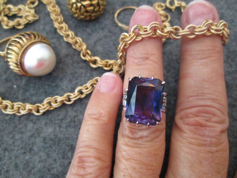 May include: A gold chain necklace with a large purple gemstone ring. The ring has a square-shaped gemstone with small diamonds around the edges.