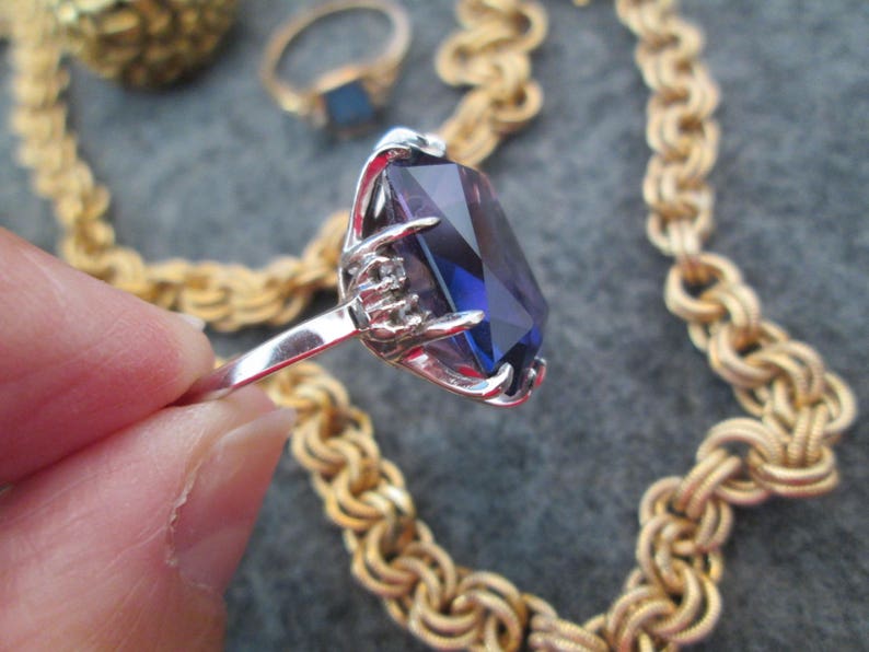 May include: A silver ring featuring a large, faceted, purple gemstone set in a claw setting. The ring is surrounded by a gold chain.