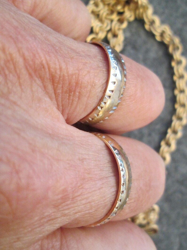 May include: Two gold wedding bands with a textured design. The bands are worn on a person's fingers.