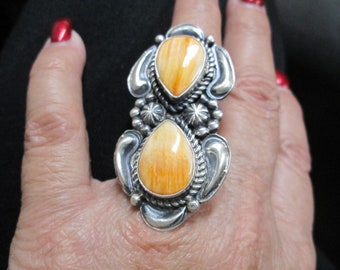 May include: A sterling silver ring with two orange and white spiny oyster shell stones. The ring has a detailed design with a rope border and a starburst pattern.