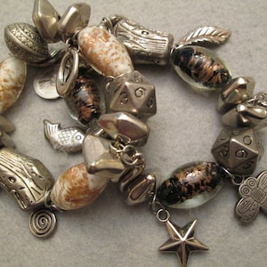 May include: A silver charm bracelet with a variety of charms, including a fish, a butterfly, a star, a key, and a dice. The bracelet also features several glass beads with a brown and white speckled pattern.