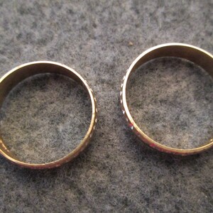 May include: Two gold-colored wedding bands with a textured pattern. The bands are simple and classic.