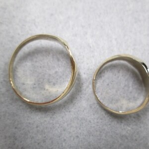 May include: Two gold-colored rings, one is wider than the other, both are smooth and shiny.