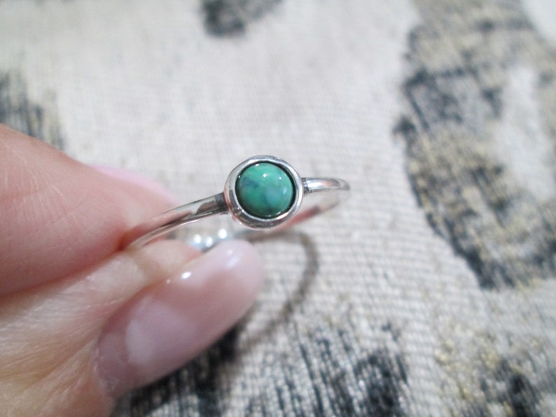 May include: A silver ring with a small, round, green gemstone.