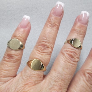 May include: Three gold signet rings with oval tops on a hand. The rings are different sizes.