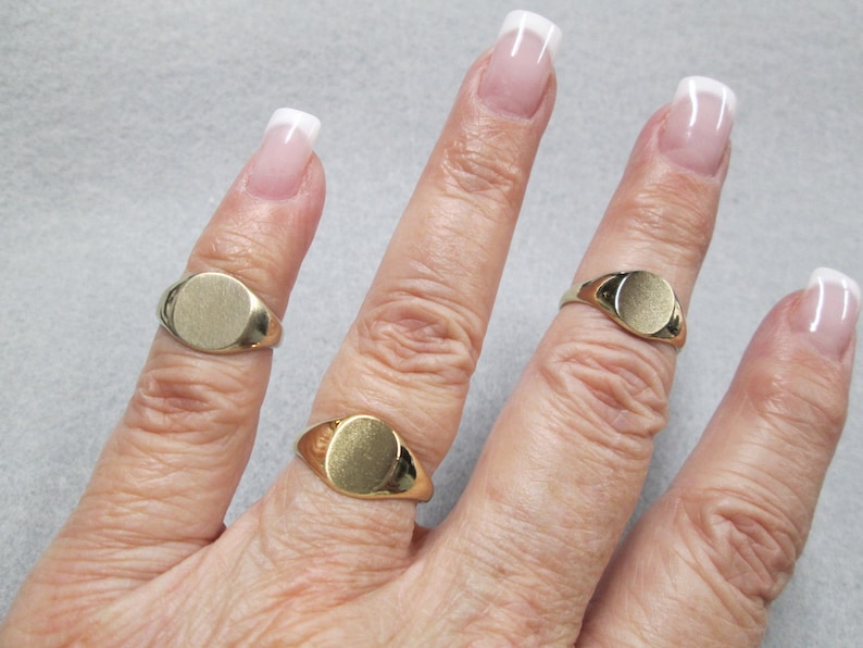 May include: Three gold signet rings with oval tops on a hand. The rings are different sizes.