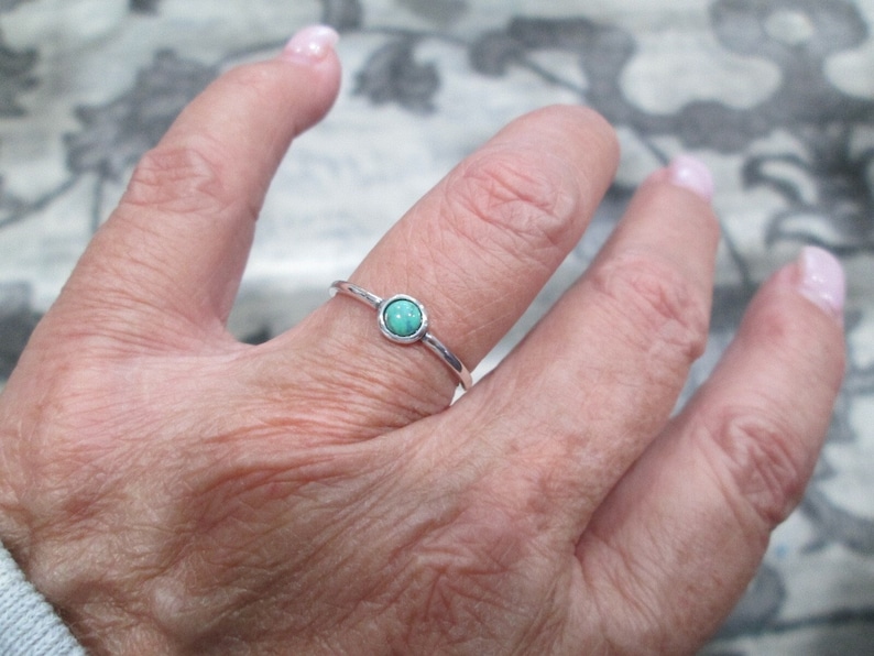 May include: A silver ring with a small, round turquoise stone.