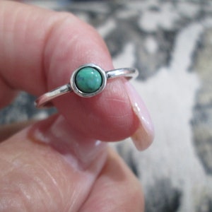 May include: A silver ring with a small, round, turquoise-colored gemstone.