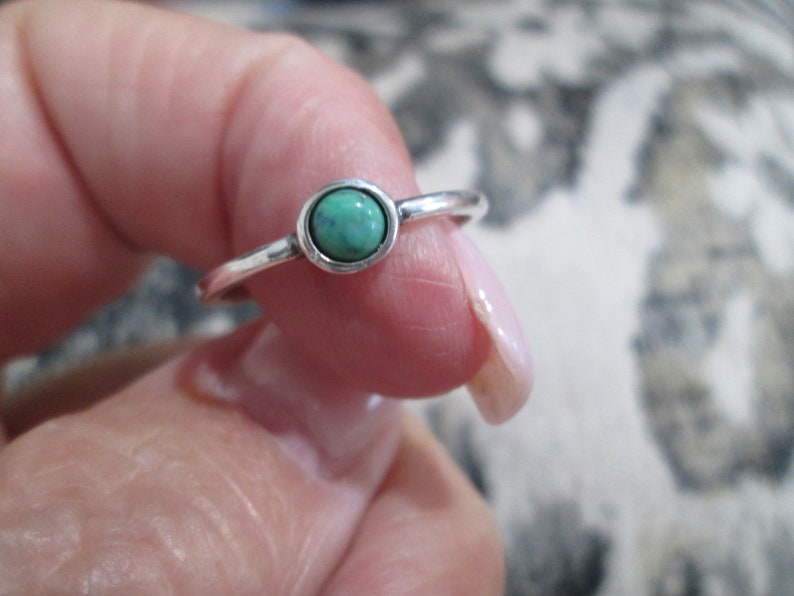 May include: A silver ring with a small, round, turquoise-colored gemstone.