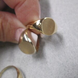 May include: Two gold signet rings with oval-shaped tops. The rings are stacked on top of each other.