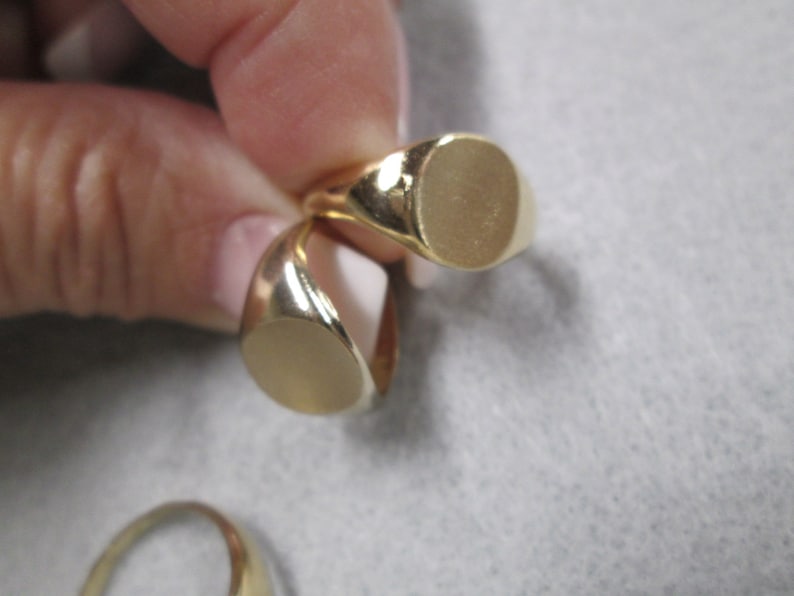 May include: Two gold signet rings with oval-shaped tops. The rings are stacked on top of each other.