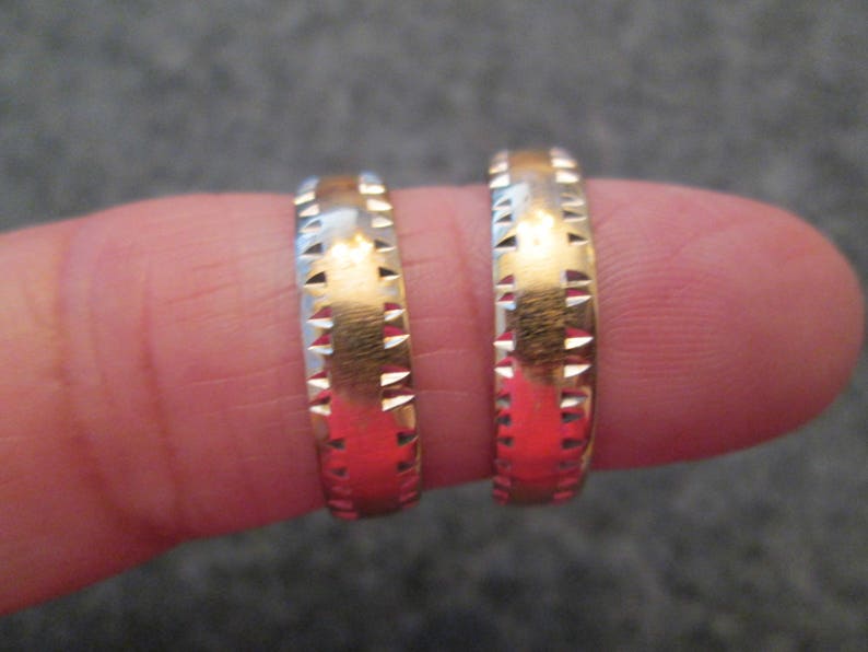 May include: Two gold wedding bands with a textured design. The bands are worn on a finger.