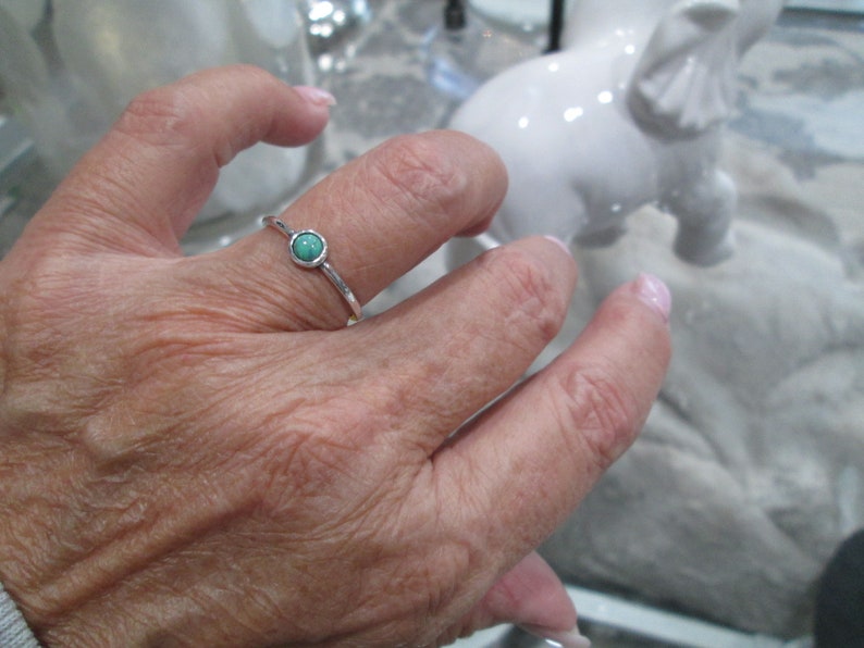 May include: A silver ring with a small, round turquoise stone set in the center.