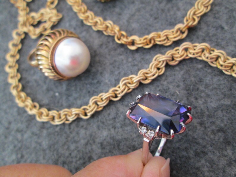 May include: A gold chain necklace with a pearl pendant and a ring featuring a large, faceted, purple gemstone with small diamond accents.