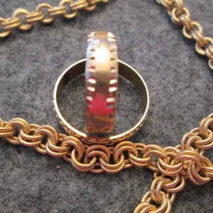 May include: Two gold rings, one with a textured band, are stacked on top of each other. The rings are lying on a gold chain.