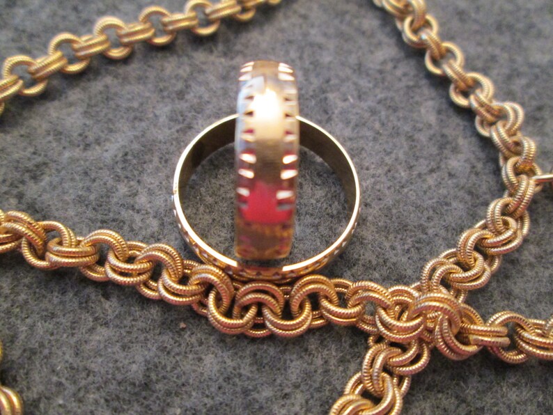 May include: Two gold rings, one with a textured band, are stacked on top of each other. The rings are lying on a gold chain.