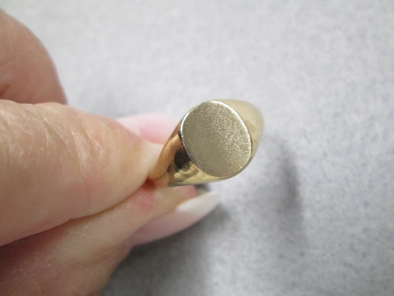 May include: A gold signet ring with a smooth, oval-shaped top.
