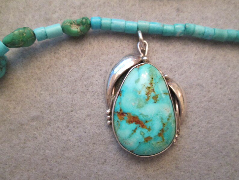 Peut inclure: Un collier avec un pendentif en turquoise serti d'argent. Le pendentif est en forme de larme avec une pierre turquoise bleue et verte. Le collier est compos&eacute; de perles turquoise.