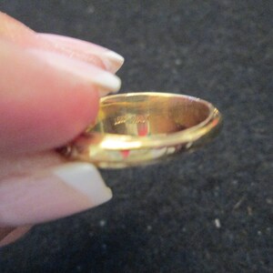 May include: A gold ring with a smooth, polished surface. The ring is held by a hand, and the interior of the ring is visible. The ring appears to be made of solid gold.