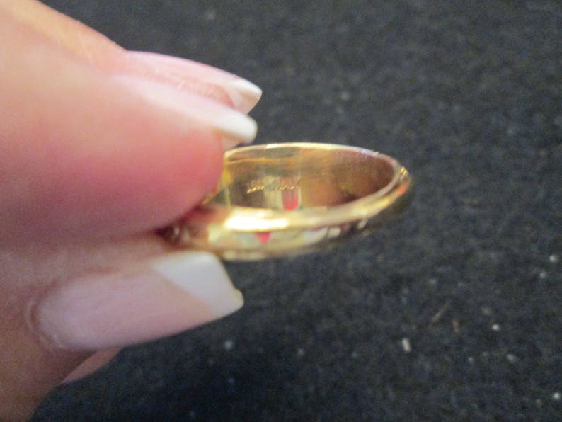 May include: A gold ring with a smooth, polished surface. The ring is held by a hand, and the interior of the ring is visible. The ring appears to be made of solid gold.