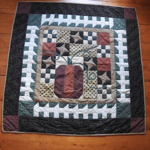 Peut inclure: Une courtepointe avec un motif de patchwork présentant une variété de couleurs et de motifs, notamment le brun, le vert, le blanc et le rouge. Le centre de la courtepointe présente une grande citrouille brodée.