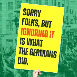 May include: A yellow sign with black text stating "SORRY FOLKS, BUT IGNORING IT IS WHAT THE GERMANS DID." The word "IGNORING" is in red. The sign is held up in front of a crowd of people.