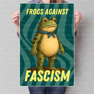May include: A poster with a cartoon frog wearing a blue scarf, standing on a brown surface. The poster has the text "FROGS AGAINST FASCISM" in yellow, with a teal background. The frog is green with a yellow belly.
