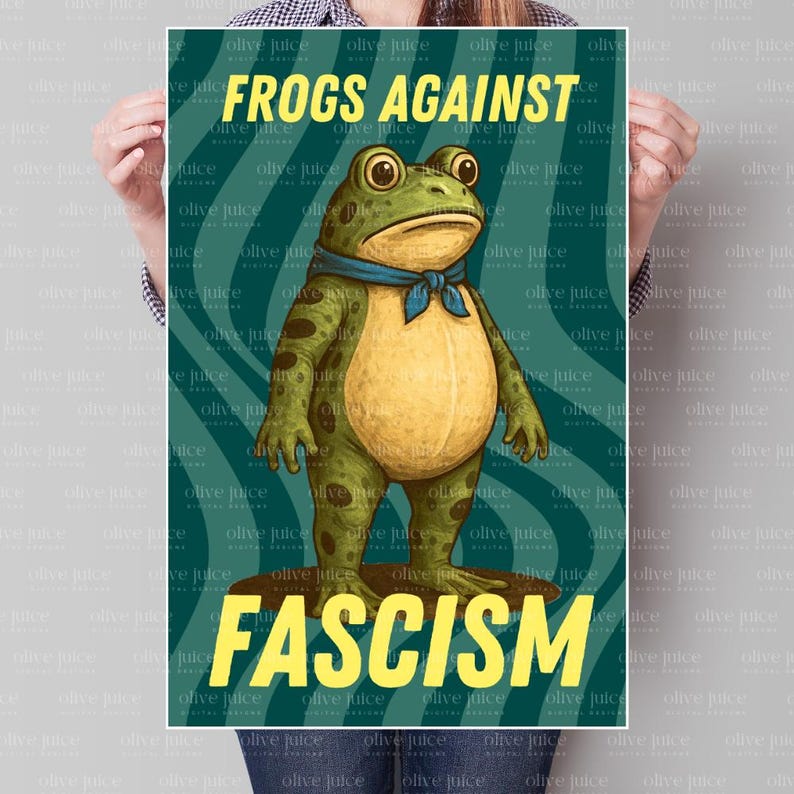 May include: A poster with a cartoon frog wearing a blue scarf, standing on a brown surface. The poster has the text "FROGS AGAINST FASCISM" in yellow, with a teal background. The frog is green with a yellow belly.
