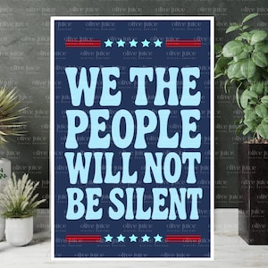 May include: A navy blue poster with the text "WE THE PEOPLE WILL NOT BE SILENT" in light blue, with red and white stripes and stars at the top and bottom. The poster has a white border and is surrounded by plants.