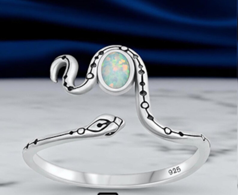 May include: A sterling silver open ring shaped like a coiled snake with a polished finish. The snake features black etched detailing along its body and a central oval-shaped iridescent opal stone. The inner band is clearly stamped with the number 925.