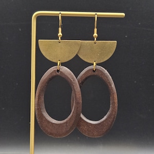 May include: A pair of dangle earrings with a brass half-circle top and a dark brown oval pendant. The earrings hang from gold-colored hooks. The background is black.