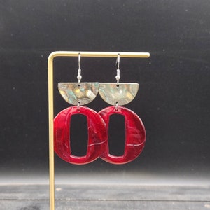 May include: A pair of red resin earrings with a silver half-moon shape at the top and a rectangular cutout in the center of each circle.
